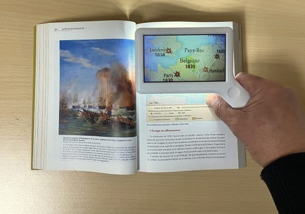La loupe de lecture AMELIE tenue à la main et positionnée au dessus d’une carte en couleur.